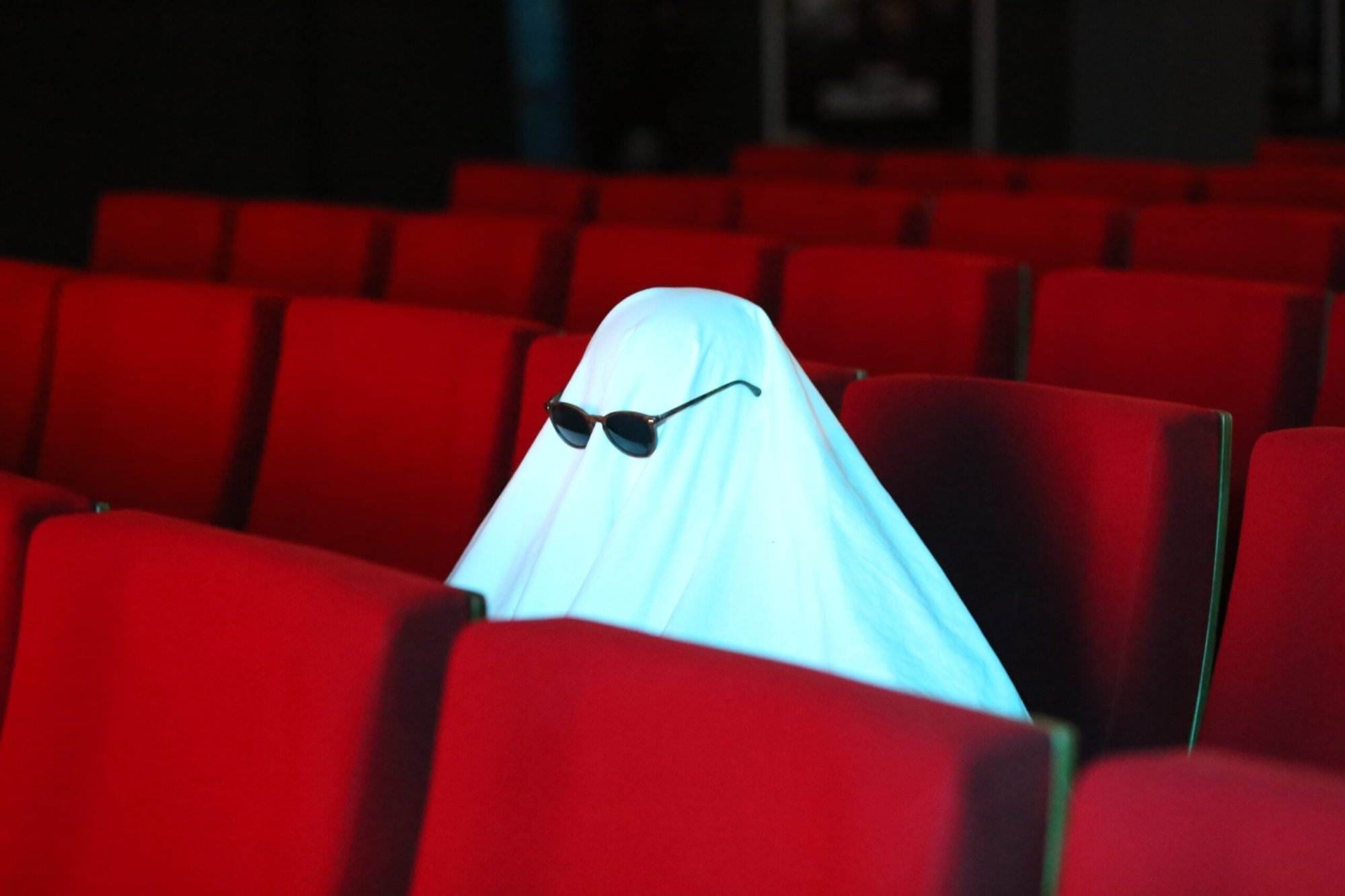 A ghost with goggles on sitting on the middle row of red seats.